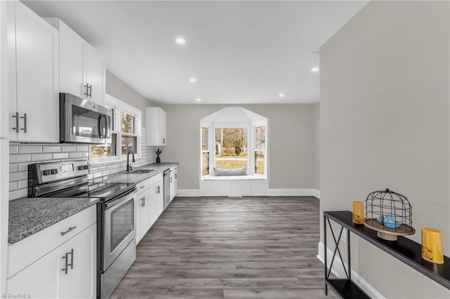 kitchen with backsplash, appliances with stainless steel finishes, white cabinetry, a sink, and wood finished floors