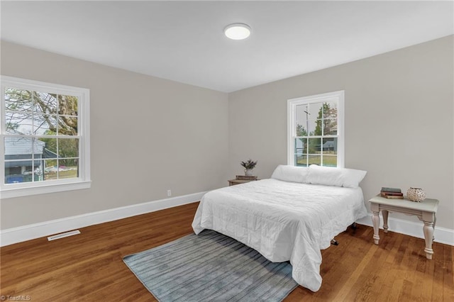 bedroom with wood finished floors, visible vents, baseboards, and multiple windows