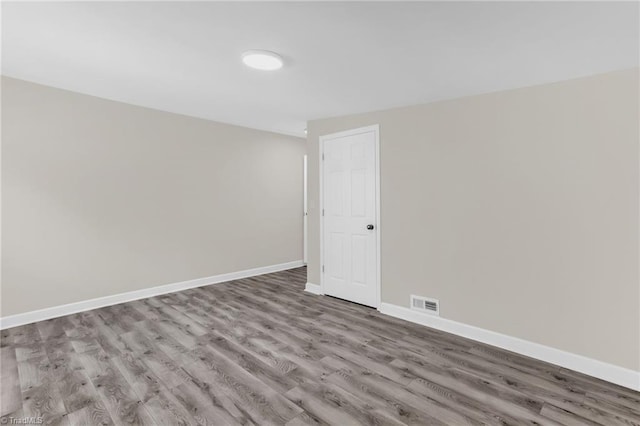 empty room featuring wood finished floors, visible vents, and baseboards