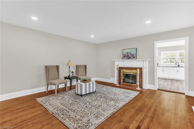 living area featuring a brick fireplace, baseboards, wood finished floors, and recessed lighting