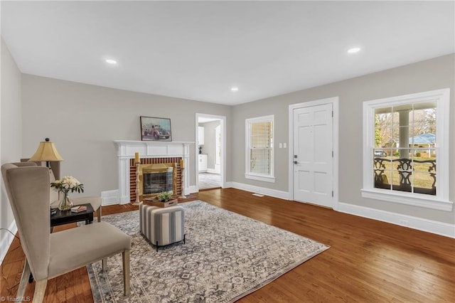 living room featuring a brick fireplace, baseboards, and wood finished floors