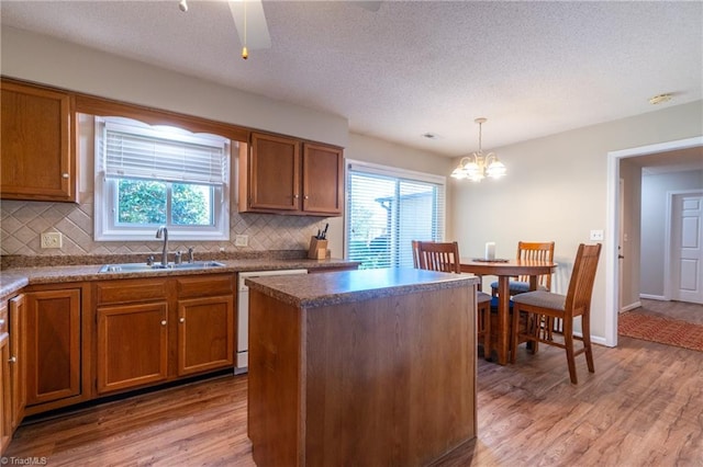 kitchen with white dishwasher, a kitchen island, sink, and light hardwood / wood-style flooring