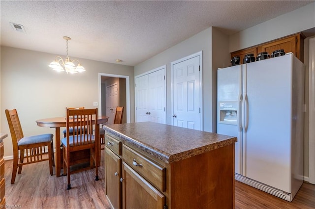 kitchen featuring a textured ceiling, white refrigerator with ice dispenser, decorative light fixtures, light hardwood / wood-style flooring, and a kitchen island