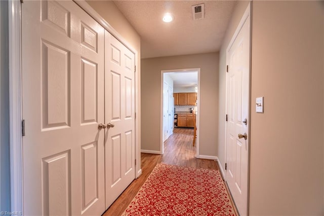 hallway featuring light wood-type flooring and a textured ceiling