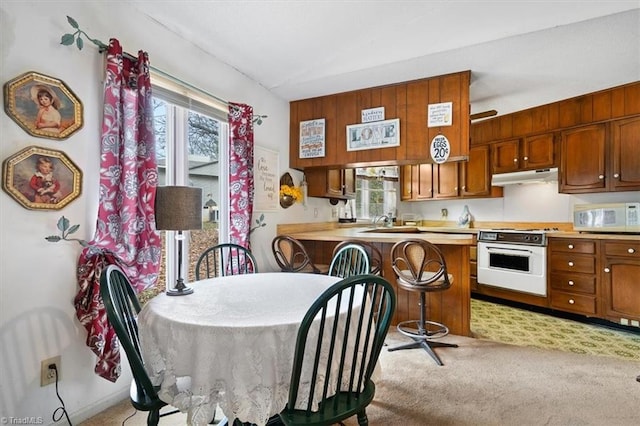 kitchen featuring a breakfast bar, kitchen peninsula, white appliances, lofted ceiling, and light colored carpet