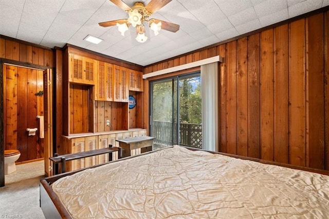 unfurnished bedroom featuring ensuite bath, access to exterior, carpet floors, wooden walls, and ceiling fan