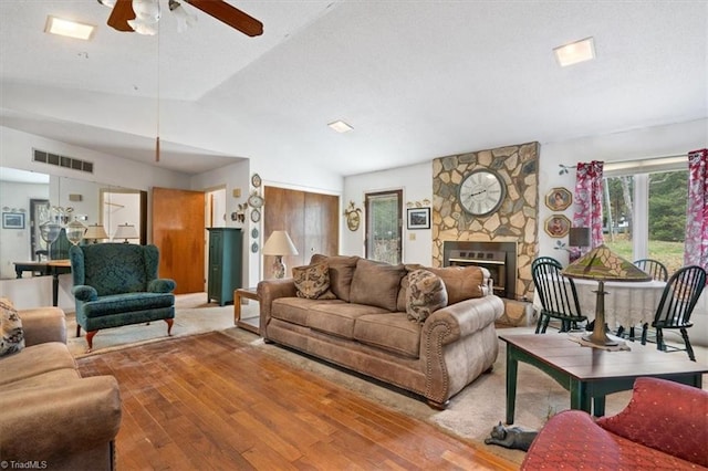 living room with ceiling fan, wood-type flooring, a stone fireplace, and vaulted ceiling