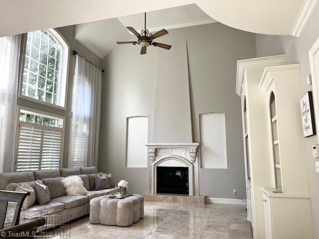 living room featuring ceiling fan, a large fireplace, and crown molding