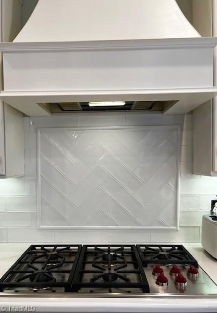 details featuring custom range hood, stove, and decorative backsplash