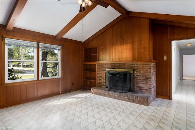 unfurnished living room with vaulted ceiling with beams, a fireplace, built in features, ceiling fan, and wooden walls