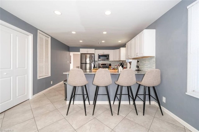 kitchen featuring light stone counters, stainless steel appliances, tasteful backsplash, white cabinets, and a kitchen bar