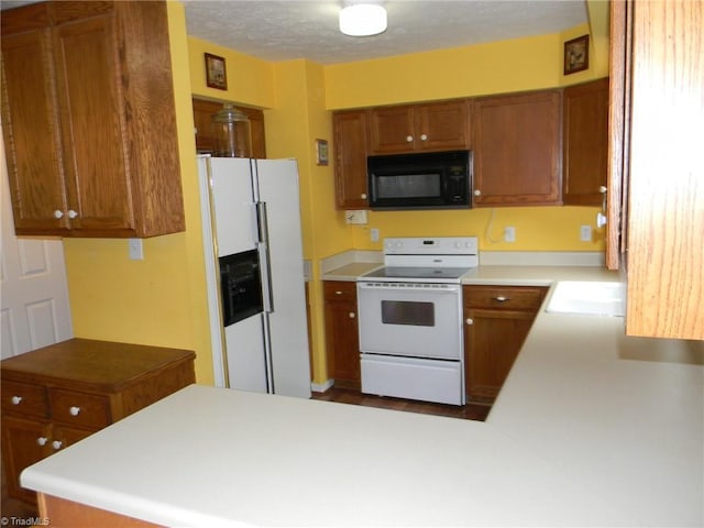 kitchen featuring light countertops, a sink, white appliances, a peninsula, and brown cabinetry