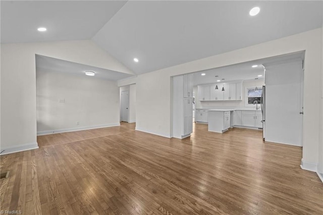 unfurnished living room with recessed lighting, baseboards, vaulted ceiling, and wood finished floors