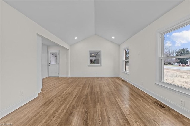 unfurnished living room with a wealth of natural light, vaulted ceiling, wood finished floors, and baseboards