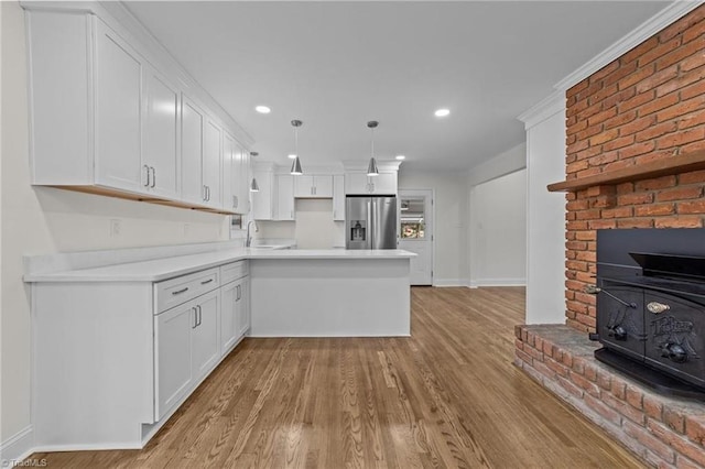 kitchen with a peninsula, white cabinets, light countertops, stainless steel fridge, and baseboards