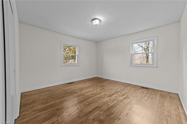 spare room with wood finished floors, baseboards, and visible vents