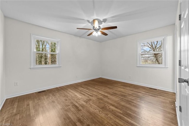 spare room featuring wood finished floors, visible vents, ceiling fan, and plenty of natural light