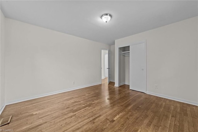 unfurnished bedroom featuring visible vents, baseboards, a closet, and wood finished floors