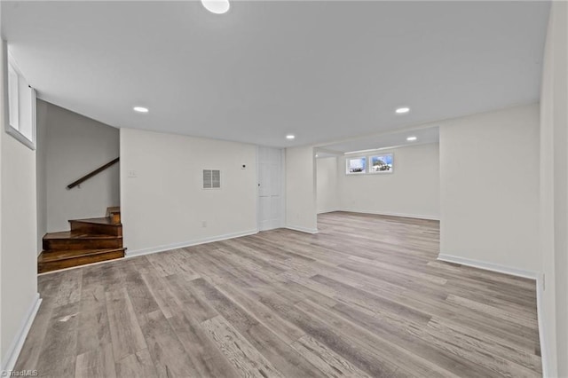 below grade area with visible vents, light wood-type flooring, stairway, and baseboards