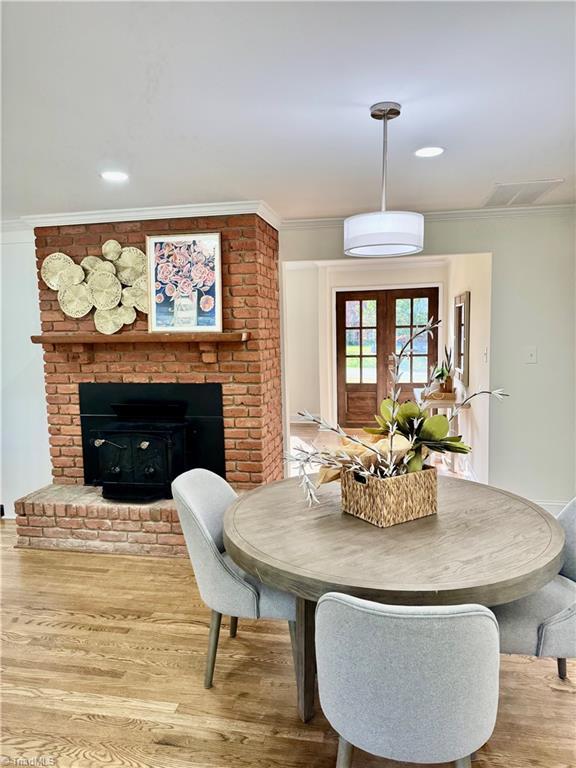 dining space with crown molding, wood finished floors, visible vents, and a brick fireplace