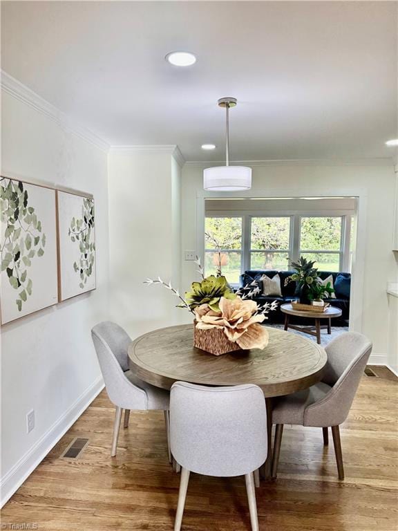dining room with crown molding, light wood finished floors, baseboards, and visible vents