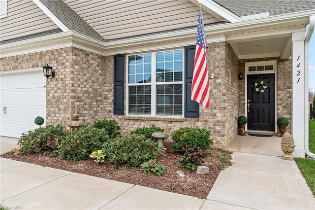 doorway to property featuring an attached garage, brick siding, and roof with shingles