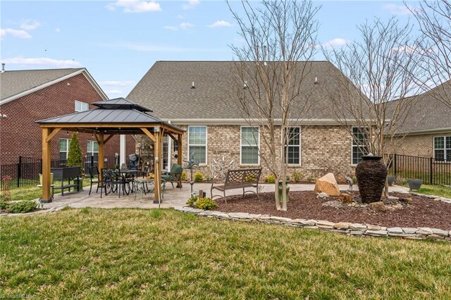 rear view of house featuring a gazebo, brick siding, a yard, and fence