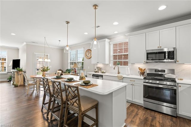 kitchen with ornamental molding, a kitchen island, stainless steel appliances, a breakfast bar area, and light countertops