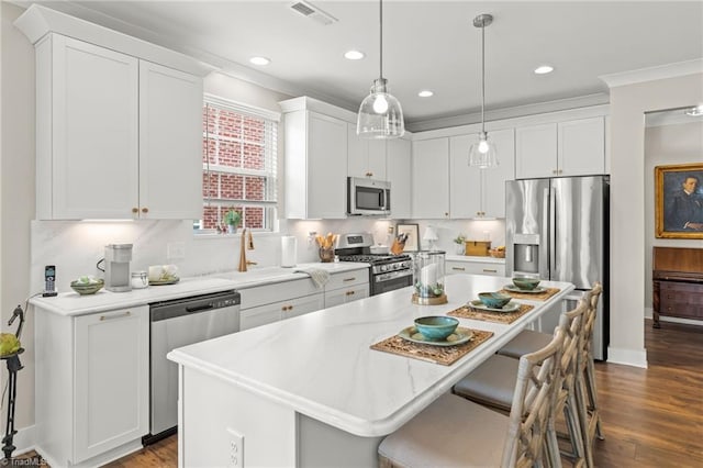 kitchen with a breakfast bar area, visible vents, a kitchen island, appliances with stainless steel finishes, and white cabinetry