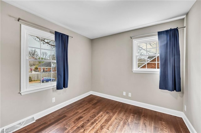 empty room with hardwood / wood-style flooring, baseboards, and visible vents