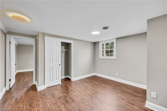 unfurnished bedroom with a closet, baseboards, visible vents, and dark wood-style flooring