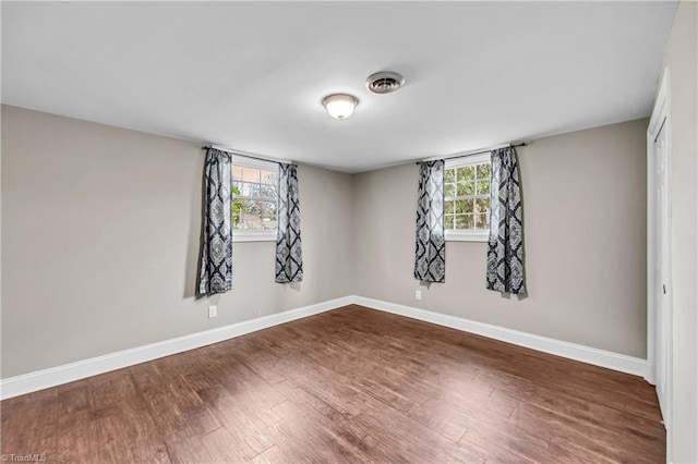 empty room with baseboards, dark wood-type flooring, and plenty of natural light