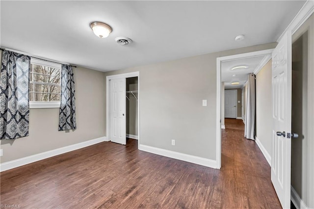 unfurnished bedroom with visible vents, baseboards, dark wood-type flooring, and a closet