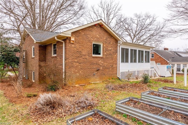 view of side of home featuring brick siding, a vegetable garden, and a sunroom