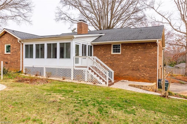 rear view of house with a yard, a sunroom, a shingled roof, a chimney, and brick siding