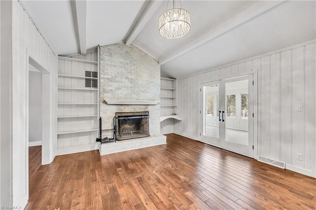 unfurnished living room featuring visible vents, a brick fireplace, lofted ceiling with beams, hardwood / wood-style floors, and an inviting chandelier