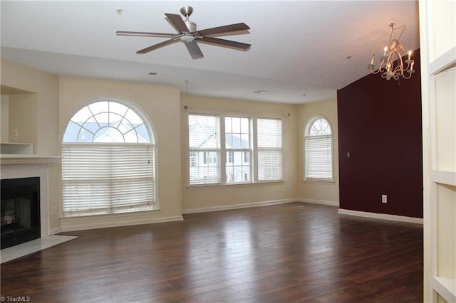 unfurnished living room with ceiling fan with notable chandelier, a tile fireplace, and dark wood-type flooring