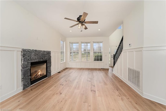 unfurnished living room featuring stairway, visible vents, a stone fireplace, a decorative wall, and light wood-type flooring