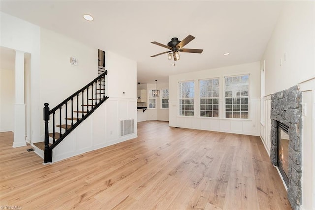 unfurnished living room featuring light wood-type flooring, visible vents, stairway, a fireplace, and ceiling fan