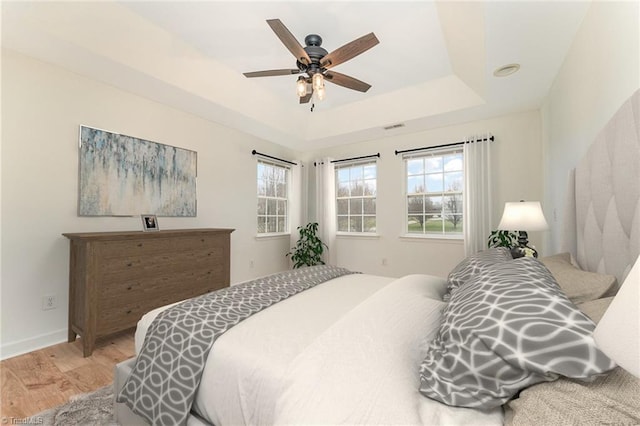 bedroom featuring visible vents, baseboards, light wood-style floors, a raised ceiling, and a ceiling fan