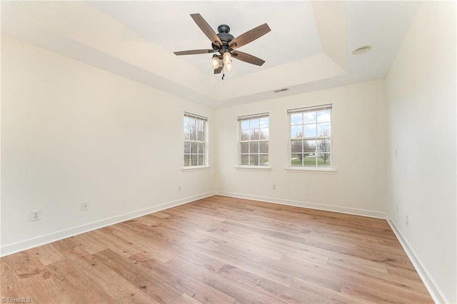 spare room with a tray ceiling, light wood-style floors, visible vents, and baseboards