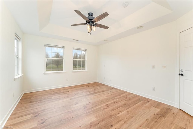 empty room with baseboards, a raised ceiling, light wood-style floors, and ceiling fan