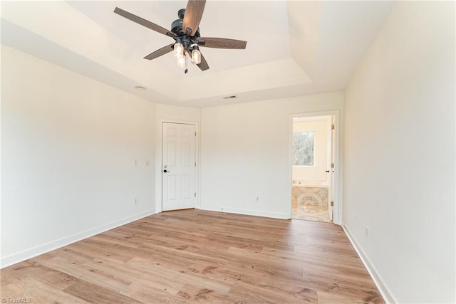 empty room featuring light wood-type flooring, a tray ceiling, baseboards, and ceiling fan