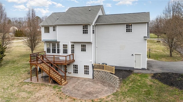 back of property featuring a lawn, a deck, stairway, roof with shingles, and a patio area