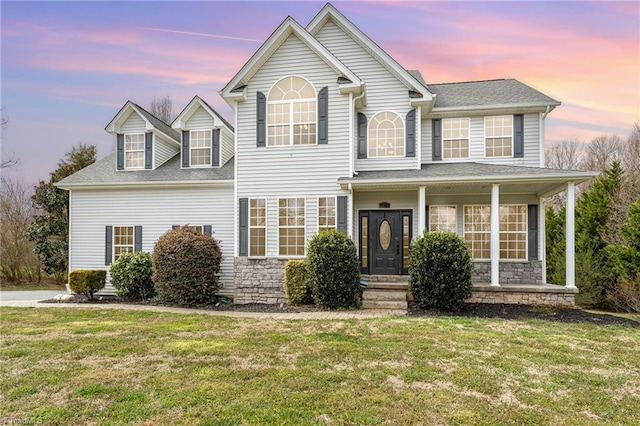 view of front of house featuring stone siding, covered porch, a shingled roof, and a front yard