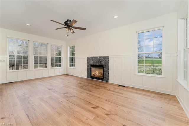 unfurnished living room featuring a ceiling fan, visible vents, a fireplace, a decorative wall, and light wood-type flooring