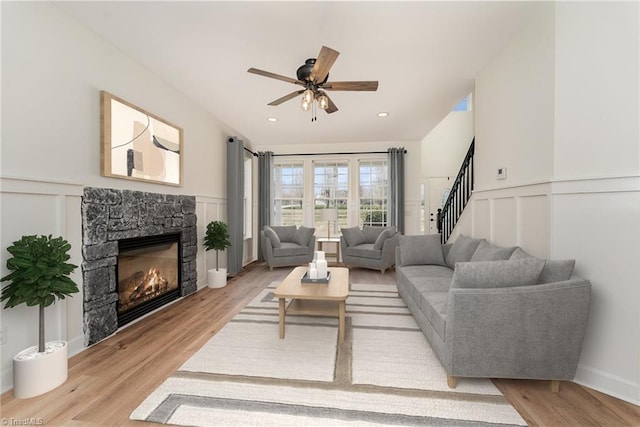 living room featuring stairway, a stone fireplace, light wood-style flooring, and a decorative wall