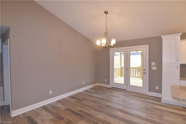 unfurnished dining area with a notable chandelier, vaulted ceiling, baseboards, and wood finished floors