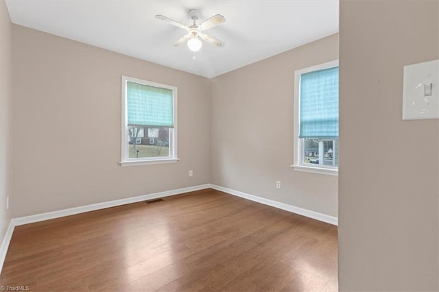 spare room featuring baseboards, plenty of natural light, wood finished floors, and a ceiling fan