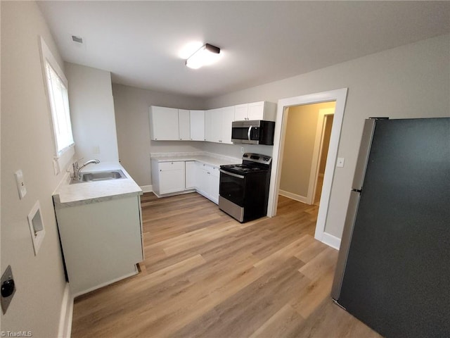 kitchen featuring light countertops, a sink, white cabinetry, stainless steel appliances, and light wood-style floors